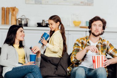 neşeli çocuğun seçici odak anne bakarak ve patlamış mısır kova ile baba yakınında gülümseyen 