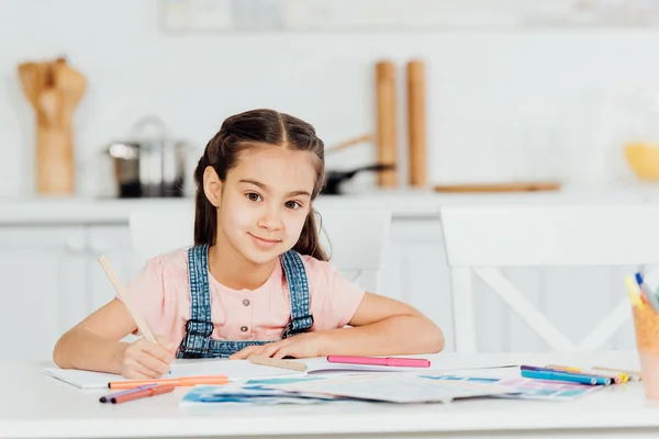 Evde Kağıt Yakınında Renkli Kalem Tutarken Kameraya Bakan Sevimli Çocuk — Stok fotoğraf