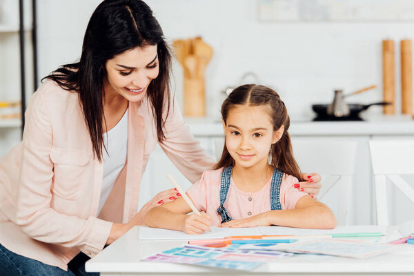 happy mother standing near paper near happy daughter looking at camera 