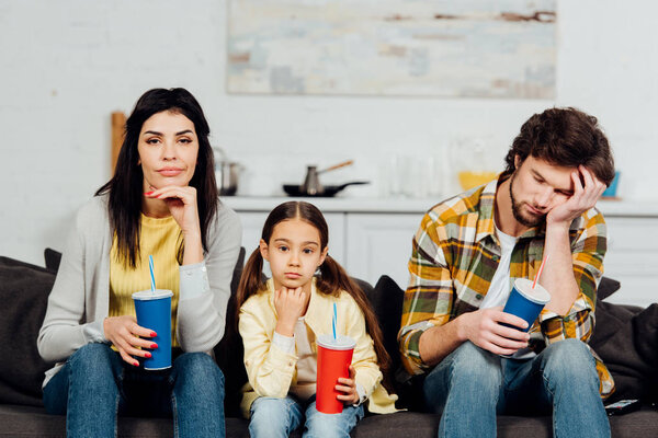 bored family holding disposable cups while watching movie at home 