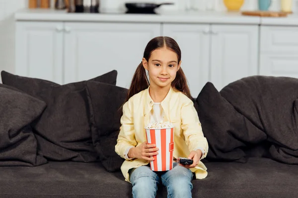 Fröhliches Kind Mit Fernbedienung Auf Sofa Mit Eimer Popcorn — Stockfoto