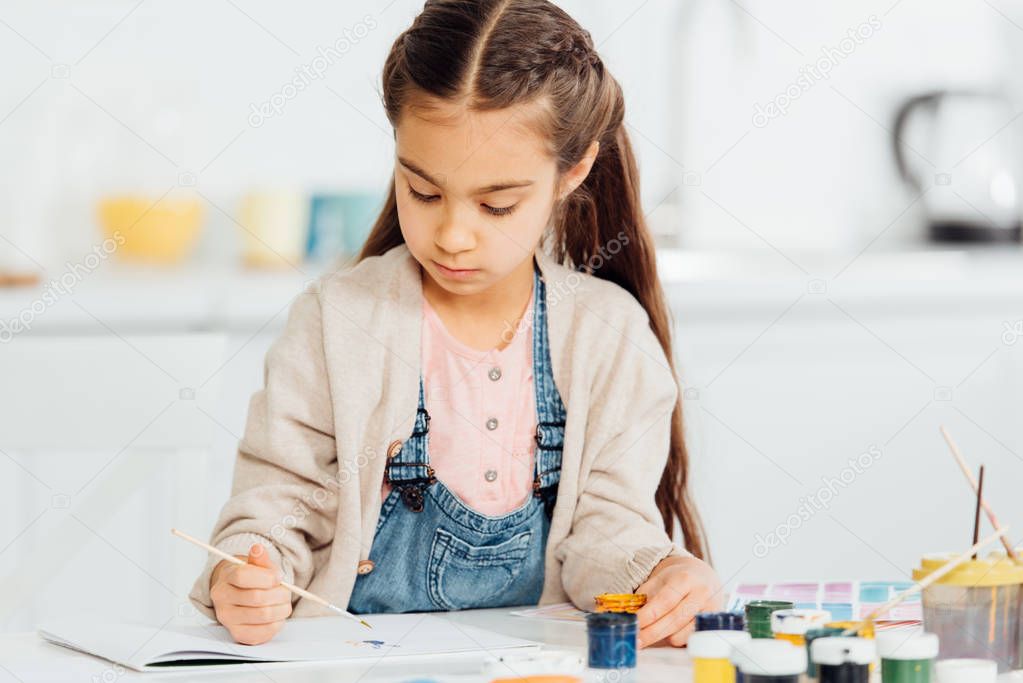 focused kid drawing with paintbrush on paper at home 