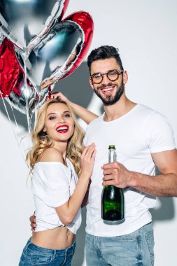 beyaz balonlar ile neşeli kadın yanında şampanya şişesi tutan gözlük sakallı adam 
