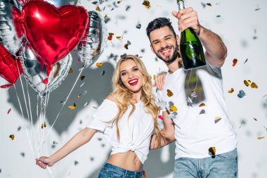 neşeli sakallı adam beyaz konfeti yakın balonlar ile kadın yakınında şampanya şişesi tutan seçici odak 