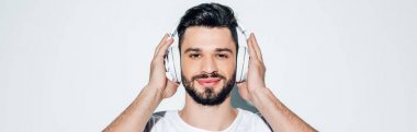 panoramic shot of cheerful man touching headphones while listening music and smiling on white  clipart