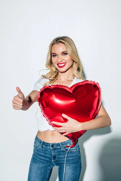 Χαρούμενο Ξανθιά Κορίτσι Κρατώντας Κόκκινο Σχήμα Καρδιάς Μπαλόνι Ενώ Δείχνοντας — Φωτογραφία Αρχείου
