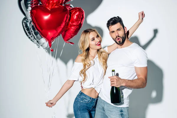 neşeli kadın balonları tutan ve beyaz şampanya şişesi ile sakallı adam bakıyor 