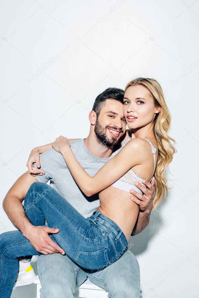 cheerful bearded man holding in arms pretty blonde woman in lace bra on white 