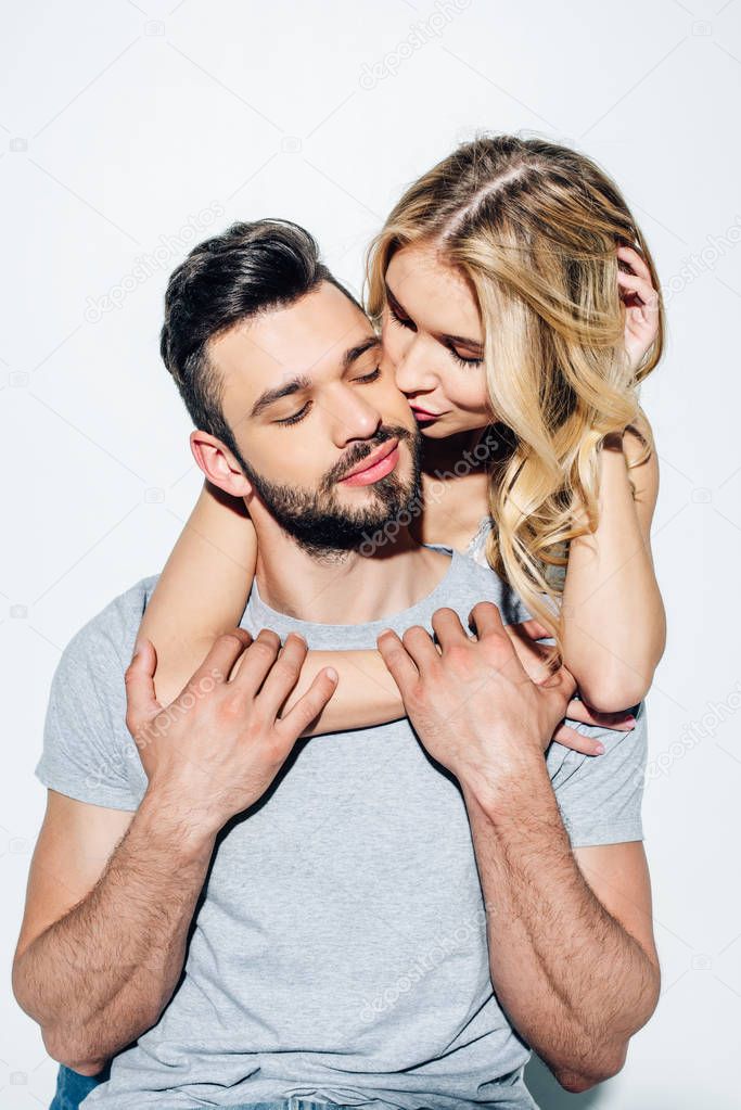 attractive blonde girl kissing cheek of handsome bearded man in white 