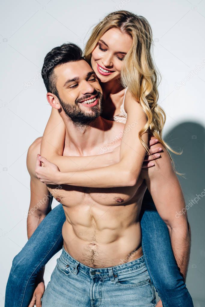 happy shirtless man piggybacking cheerful blonde woman in jeans on white 