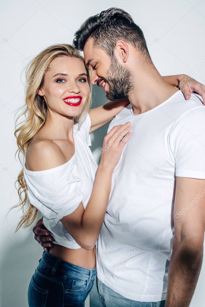 happy blonde woman hugging cheerful bearded man smiling on white 