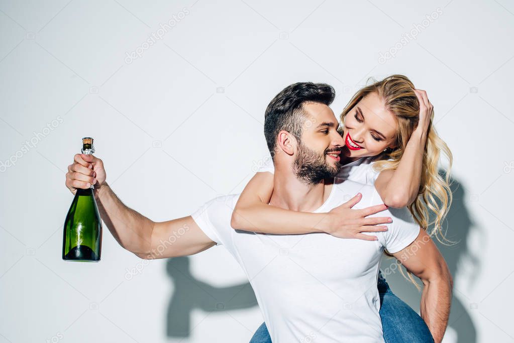 happy man holding bottle of champagne while piggybacking blonde girl on white 