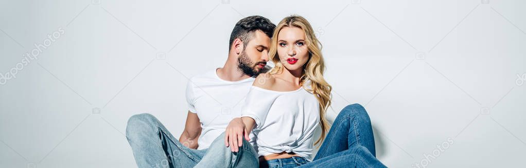 panoramic shot of handsome bearded man sitting and looking at attractive blonde girl on white 