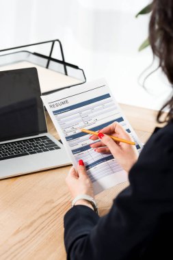 boş ekranile dizüstü bilgisayar yakınında özgeçmiş ve kalem tutan kadının seçici odak 