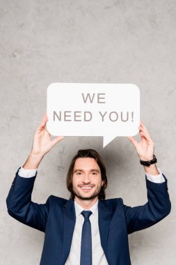 cheerful recruiter holding speech bubble with we need you lettering on grey clipart