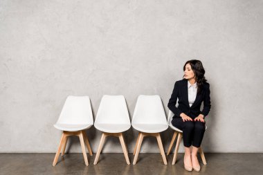 attractive brunette woman in formal wear sitting on chair before job interview  clipart