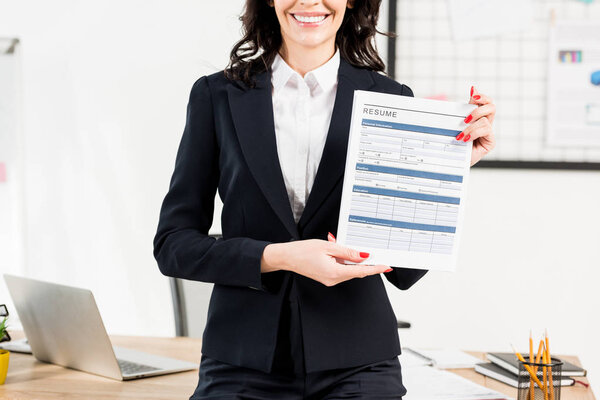 cropped view of cheerful woman holding resume in office 