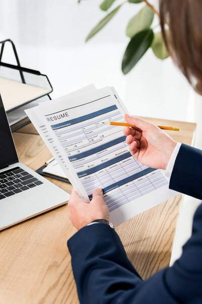 selective focus of man holding resume and pencil near laptop 