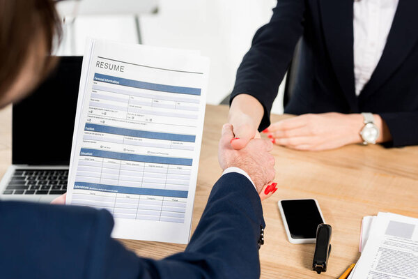 cropped view of recruiter and employee shaking hands in office 