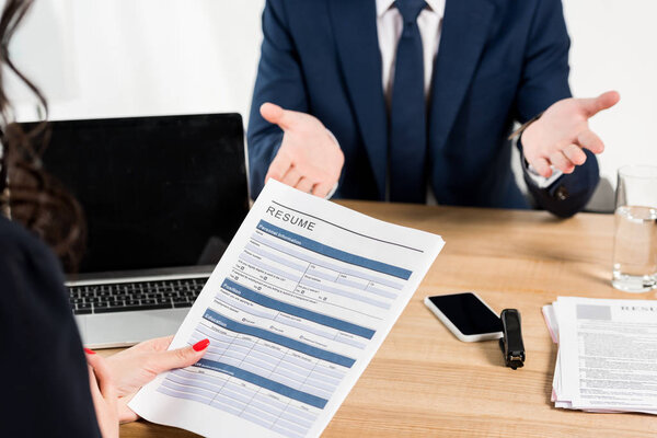 cropped view of recruiter holding resume near man gesturing in office 