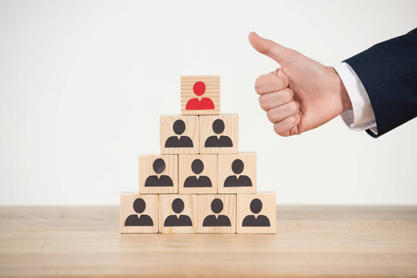 обрезанный вид человека, показывающего большой палец рядом с деревянной пирамидой кубов на белом
