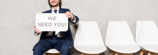 panoramic shot of recruiter sitting on chair and holding speech bubble with we need you lettering 