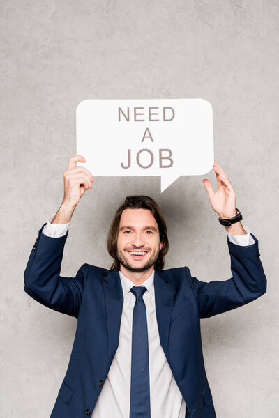 cheerful employee holding speech bubble with need a job lettering on grey