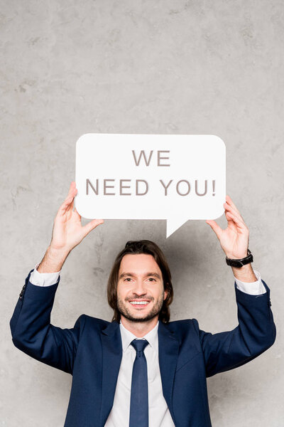 cheerful recruiter holding speech bubble with we need you lettering on grey