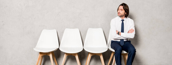 panoramic shot of handsome man sitting on chair with crossed arms and waiting job interview 