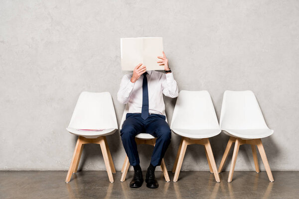 man in formal wear covering face with blank paper and sitting on chair 