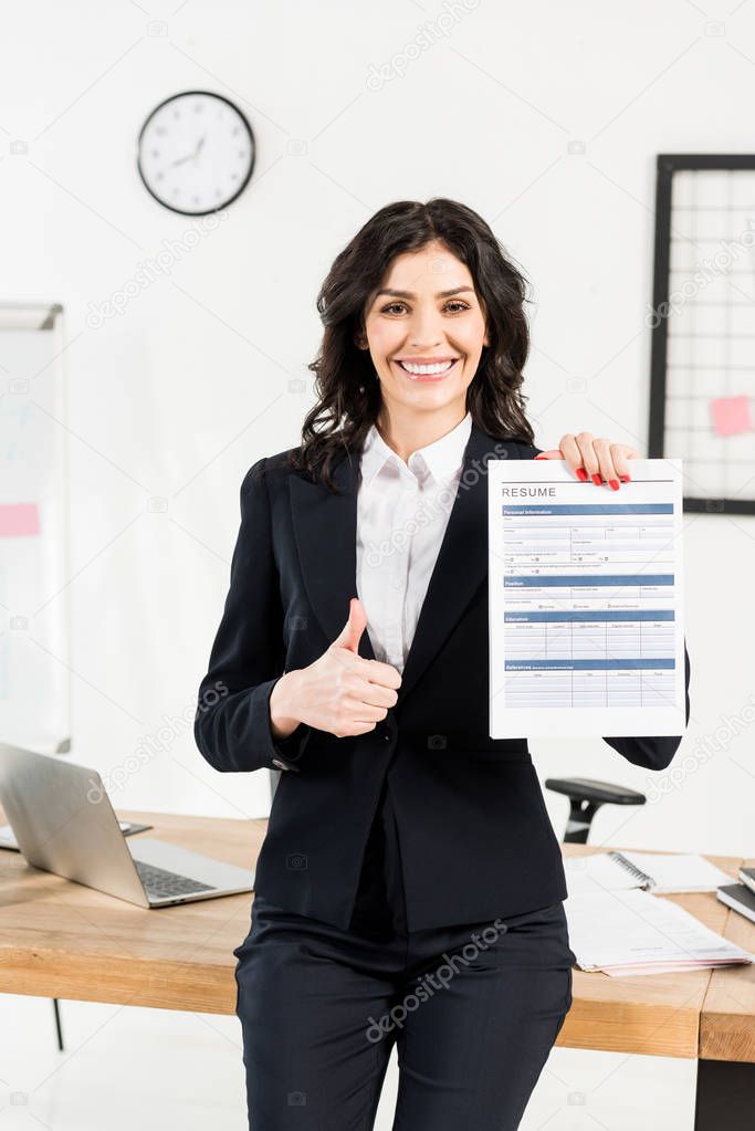 cheerful brunette recruiter holding resume and showing thumb up 