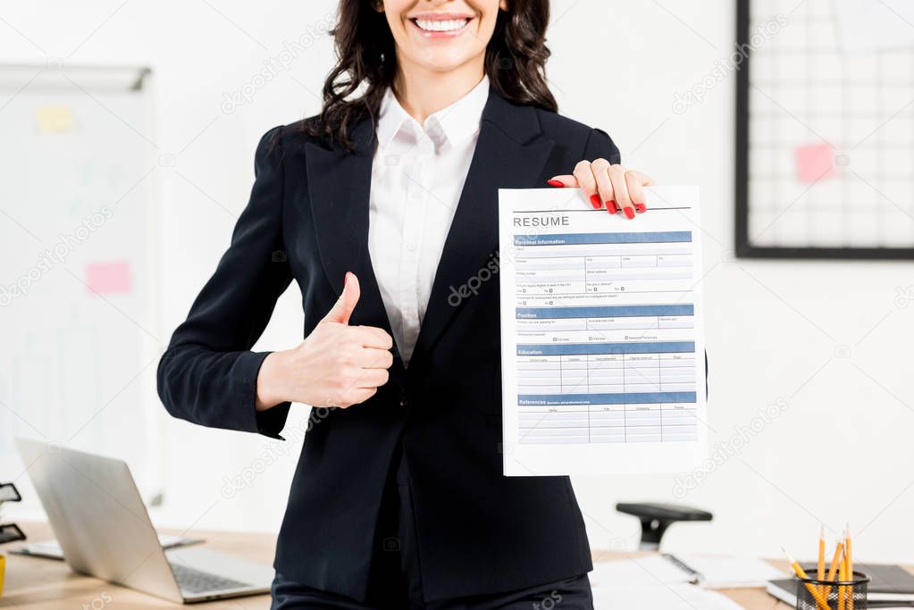 cropped view of cheerful brunette recruiter holding resume and showing thumb up 