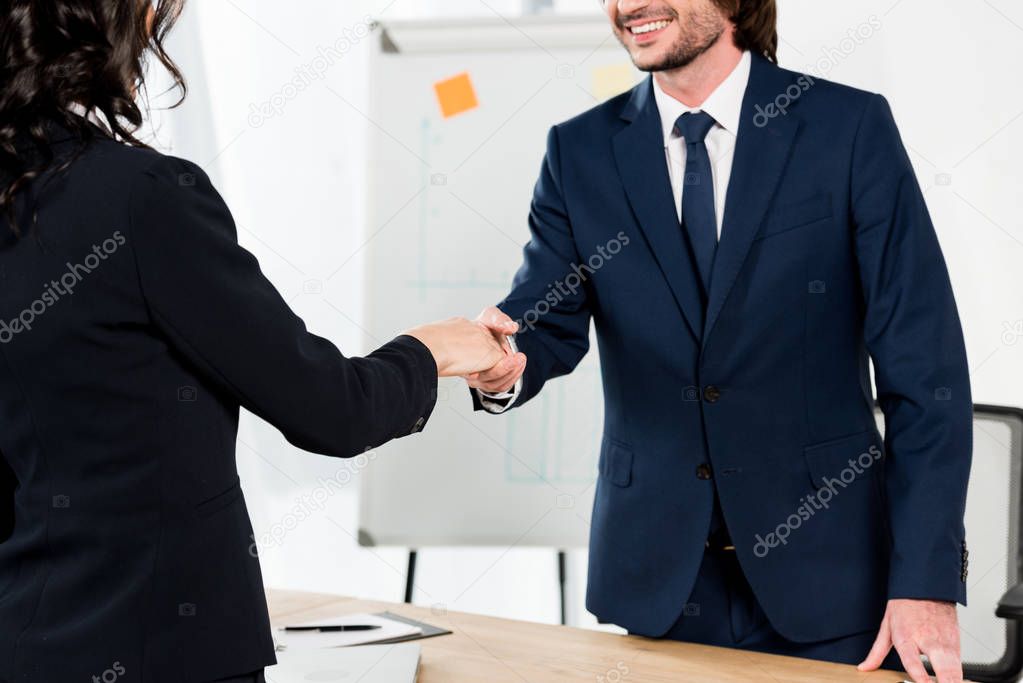 cropped view of happy recruiter shaking hands with brunette woman in office 