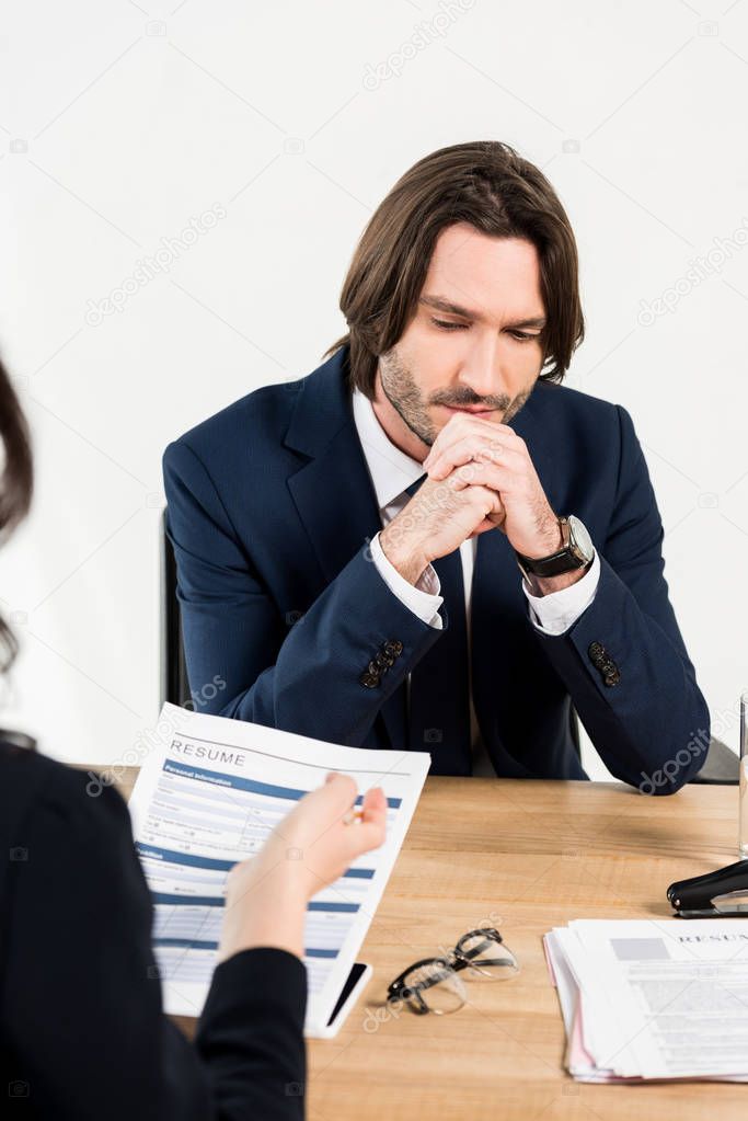 selective focus of worried man sitting with clenched hands near recruiter 
