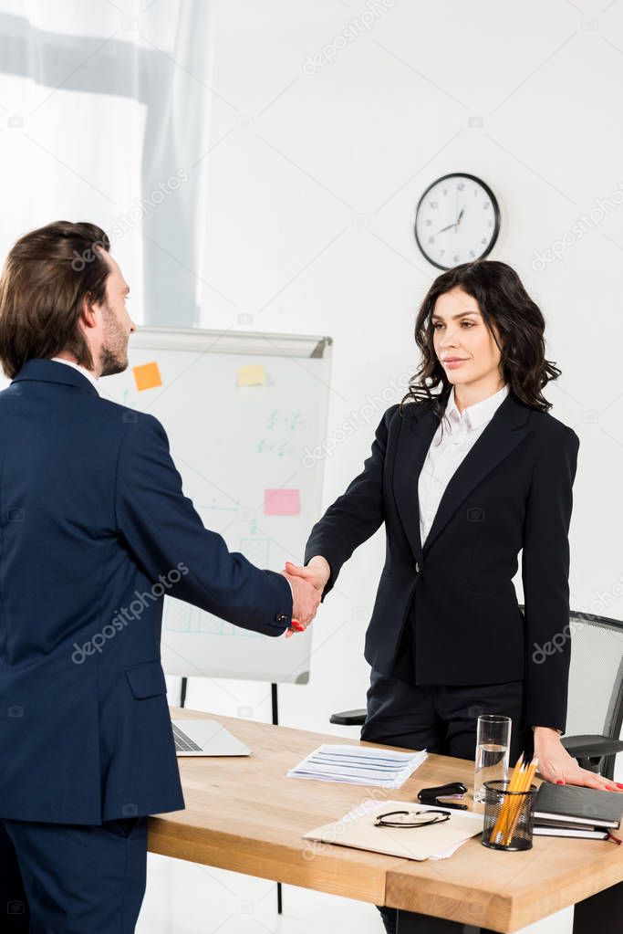 attractive brunette recruiter shaking hands with employee in office 