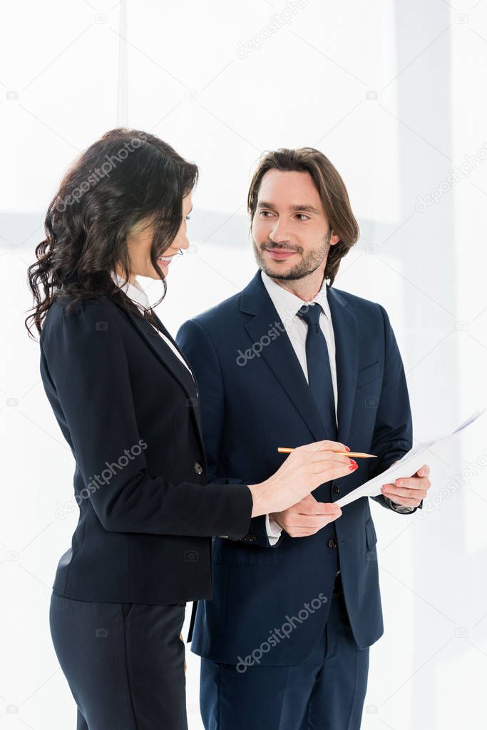 cheerful woman standing near coworker and looking at paper 