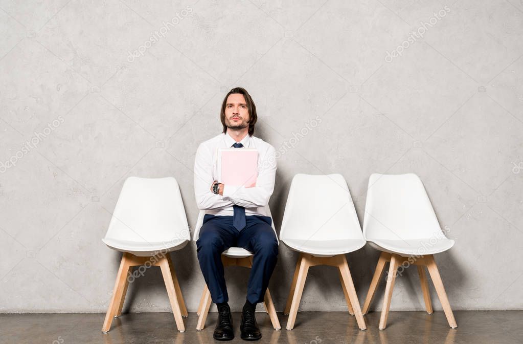 handsome man sitting on chair with crossed arms and holding folder 