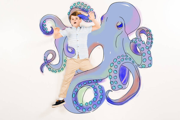 top view of scared kid gesturing near blue octopus with tentacles on white 
