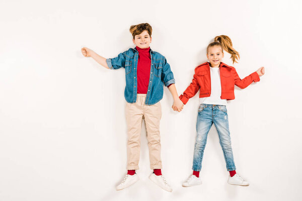 cheerful kids holding hands and smiling while lying on white 