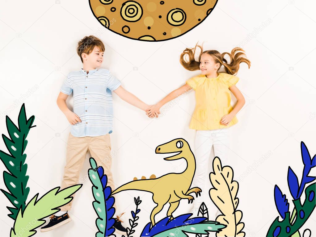 top view of cheerful kids holding hands near dinosaur on white 