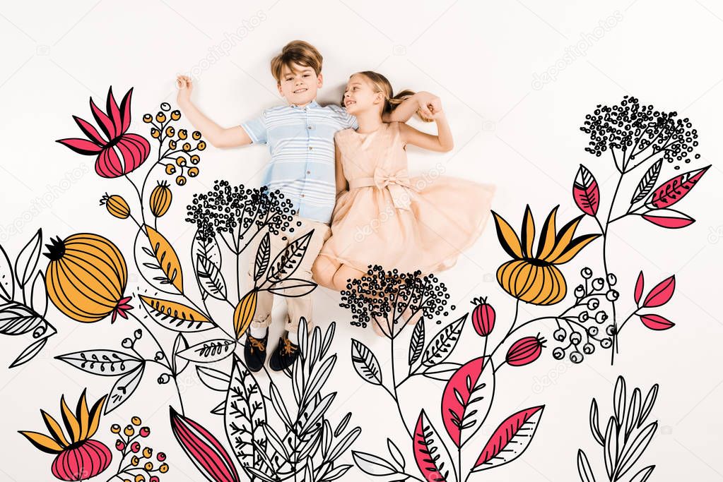 cheerful kid looking at happy friend and lying near flowers on white 