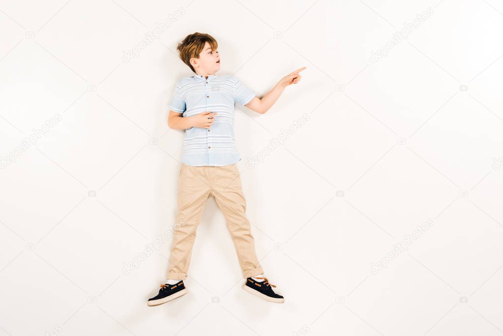 top view of surprised kid pointing with finger while lying on white 