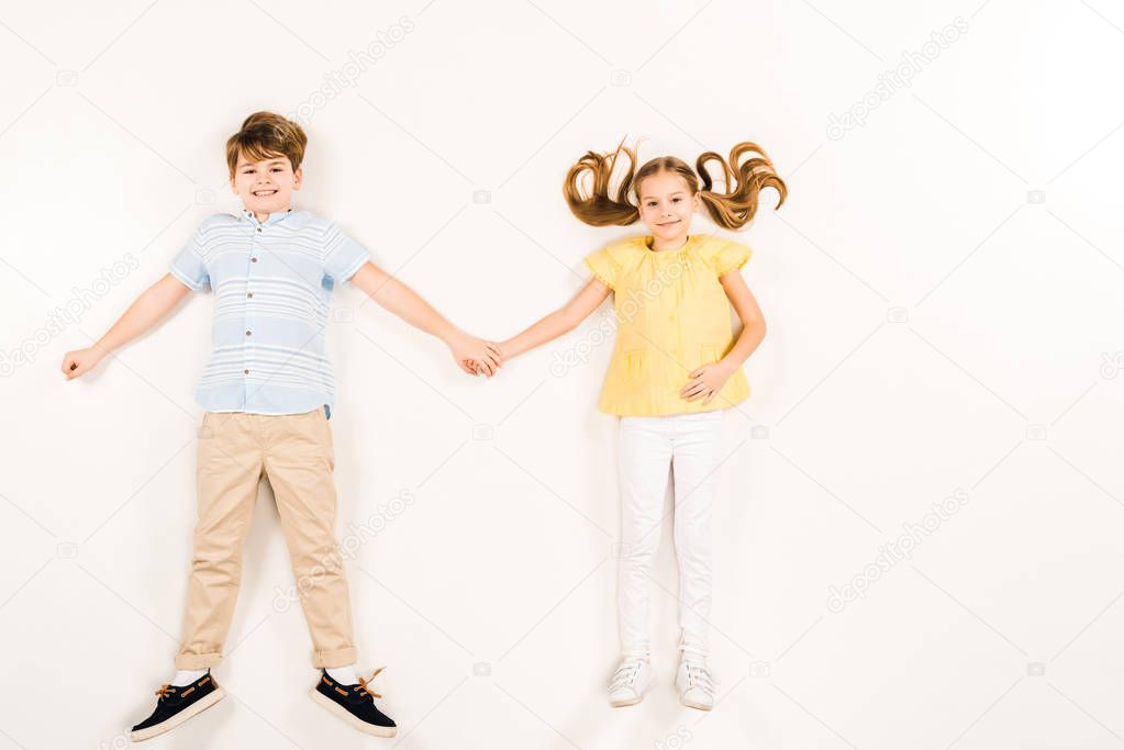 top view of cheerful kids holding hands and smiling on white 