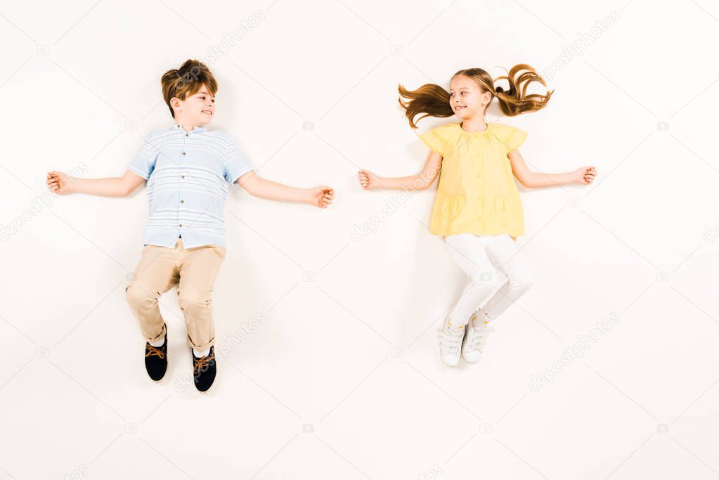 top view of cheerful kids looking at each other on white 