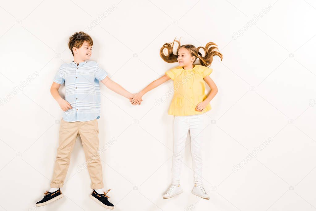 top view of cheerful kids looking at each other and holding hands on white 