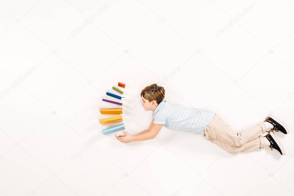 top view of cute kid holding colorful books while flying on white