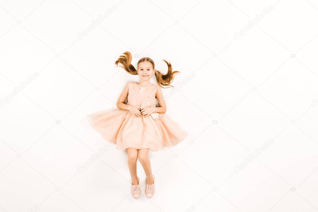 top view of happy child in pink dress looking at camera on white 