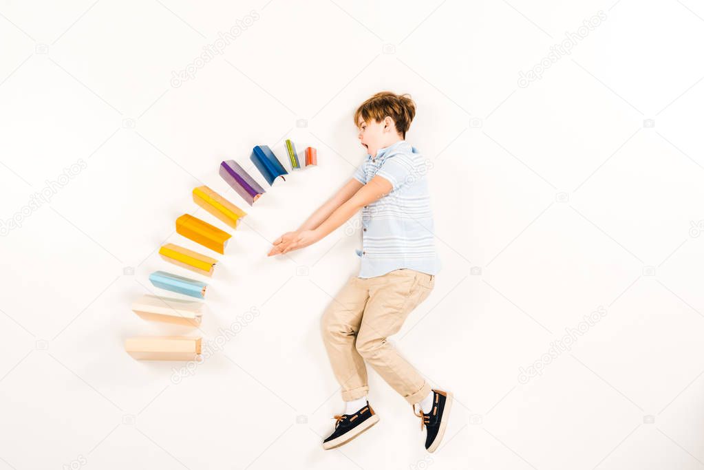 top view of surprised kid near colorful books on white 