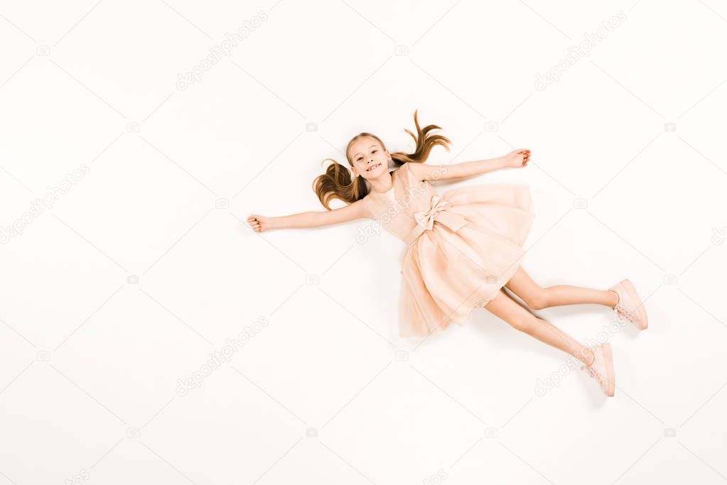 top view of smiling child in pink dress flying and looking at camera on white 