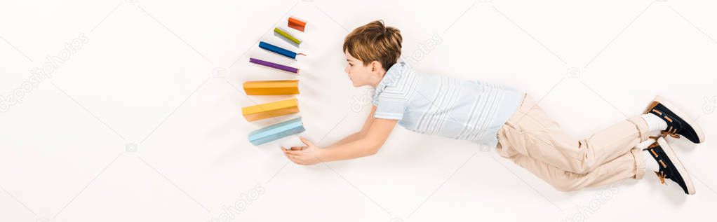 panoramic shot of cute kid holding colorful books while flying on white